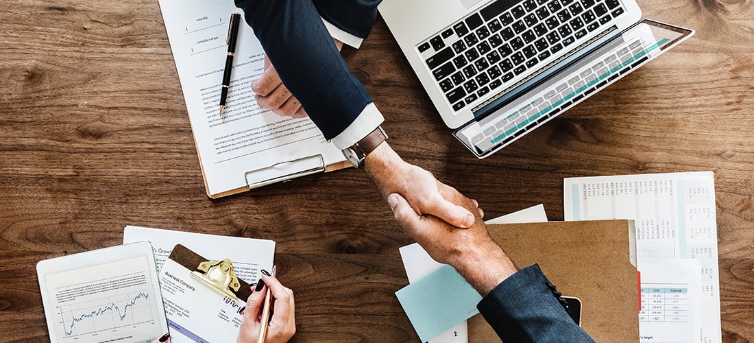 Two people shaking hands over documents